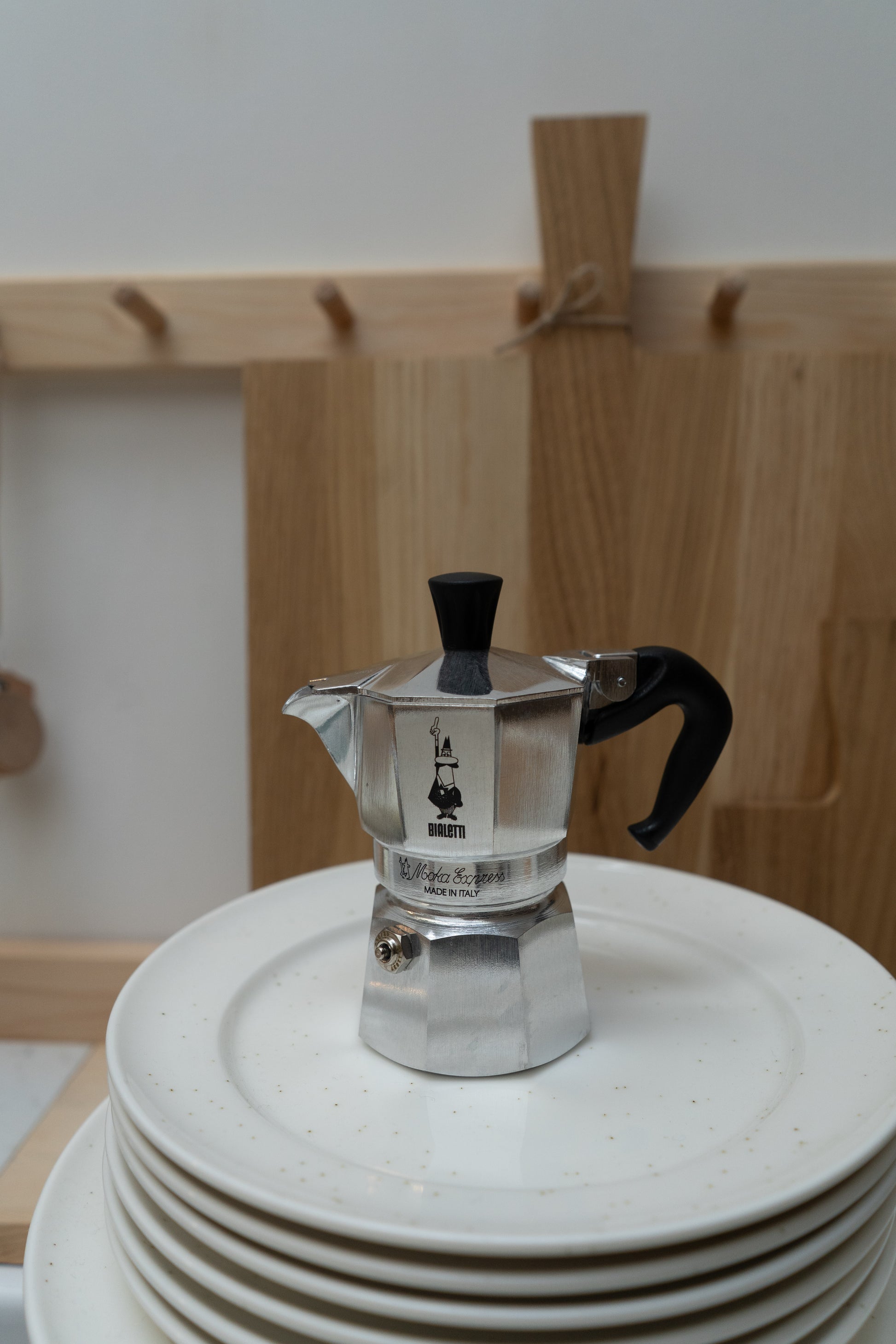 Silver espresso maker on a stack of white plates with a wooden background