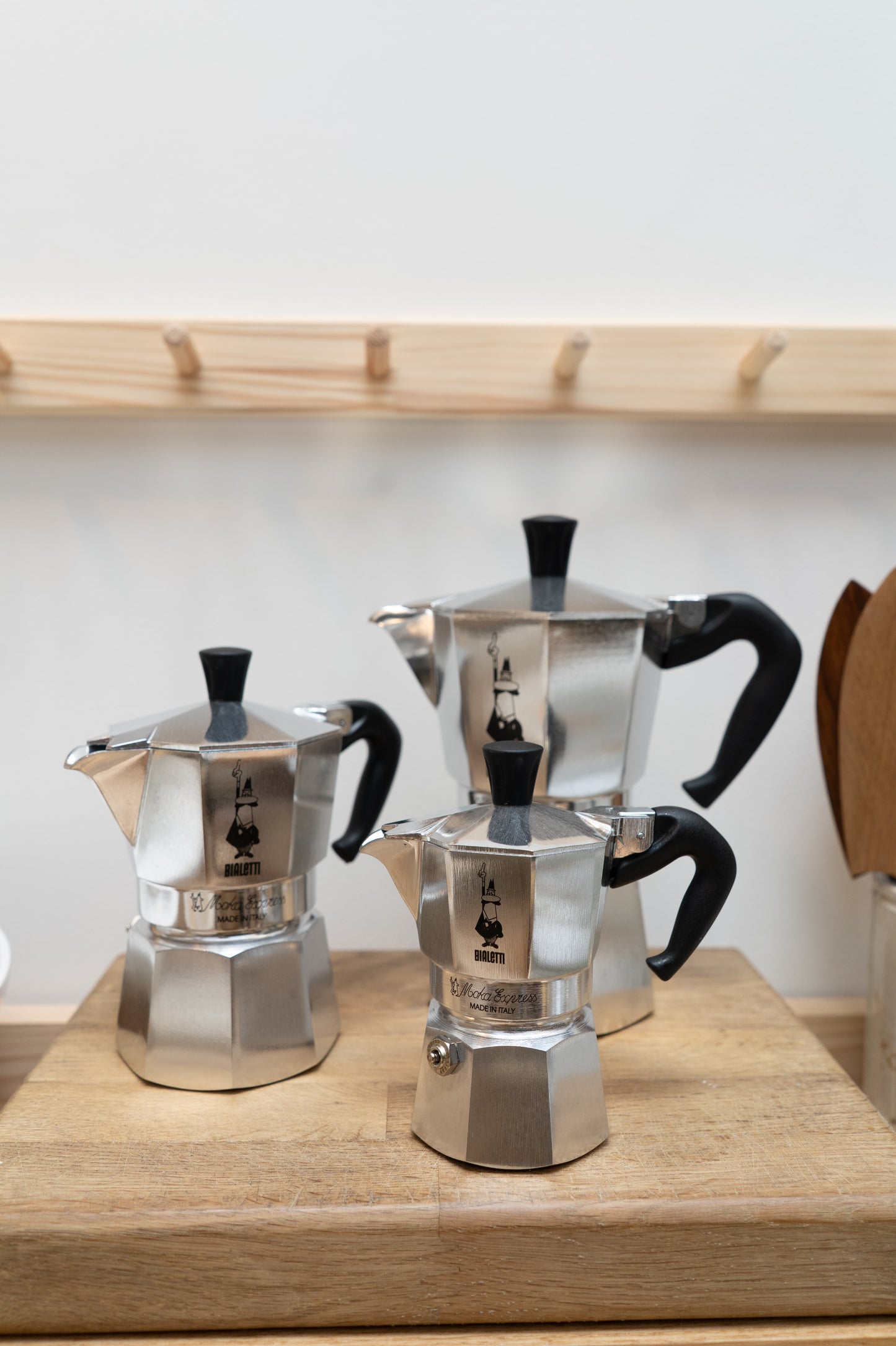 Three silver espresso pots with black handles on a wooden surface.