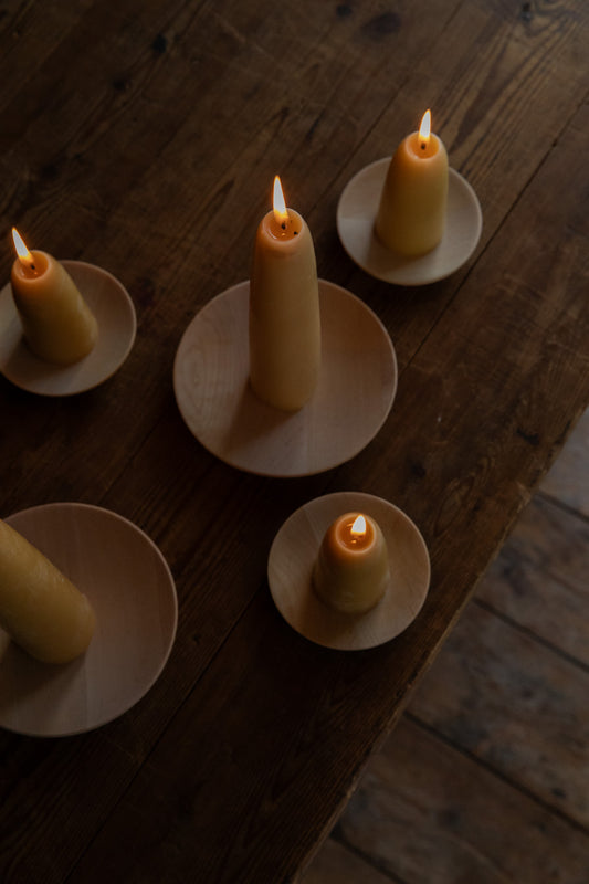 Lit beeswax candles sitting on Birch wooden plates on top of a dark wooden table.