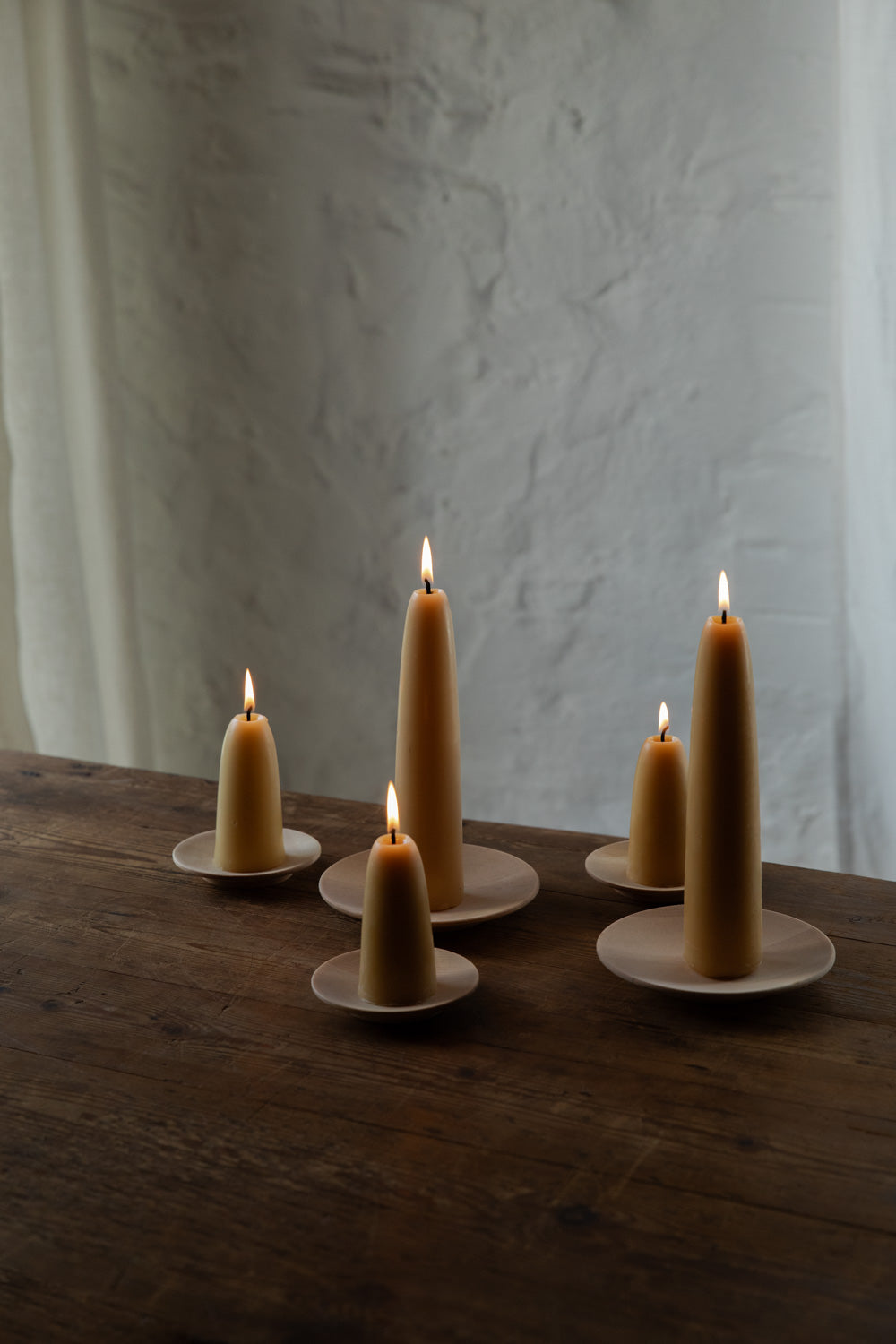 Five lit beeswax candles on Birch wood plates against a textured white wall.