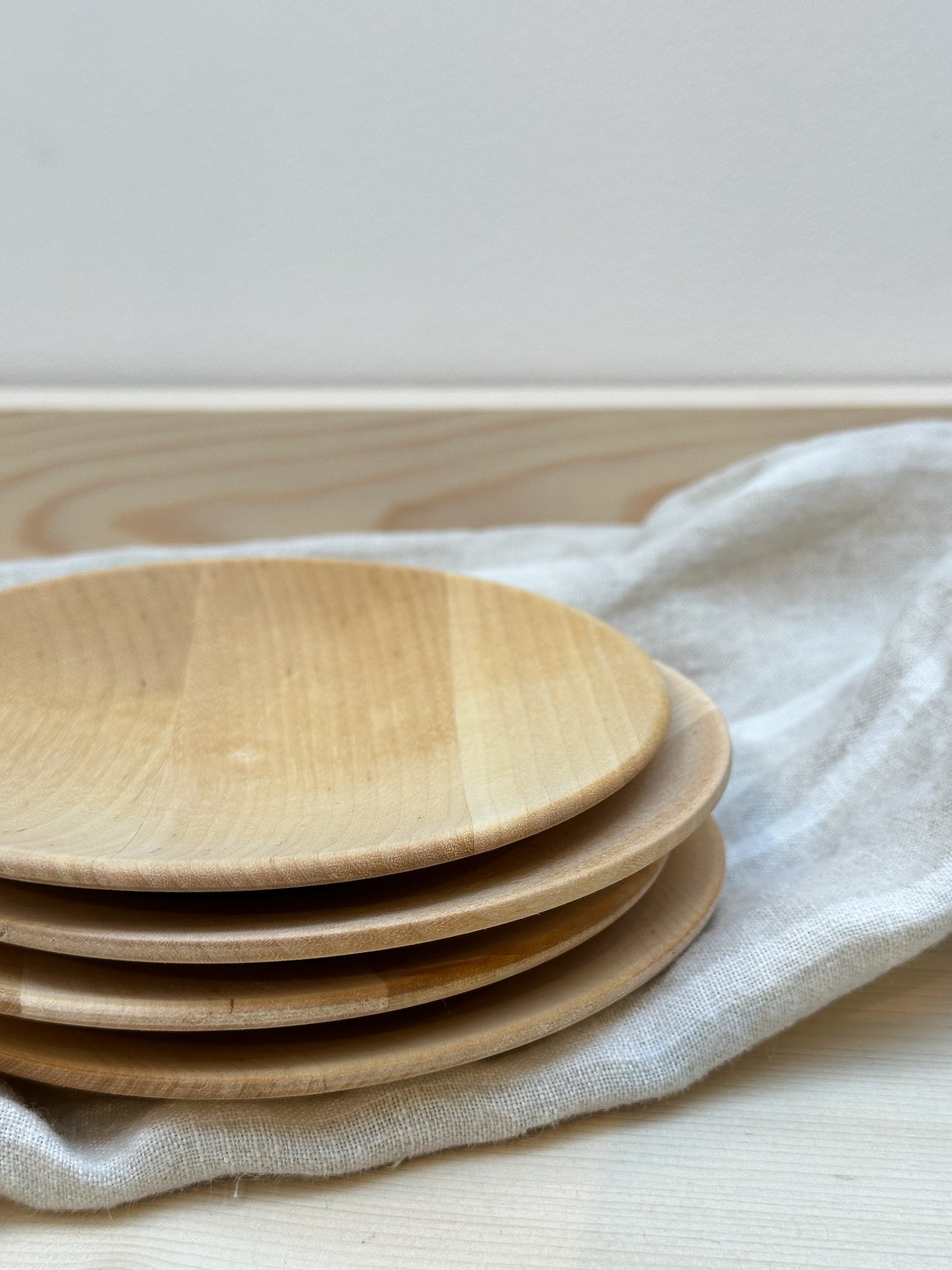 A set of four birch wood plates stacked on top of each other against a white background.