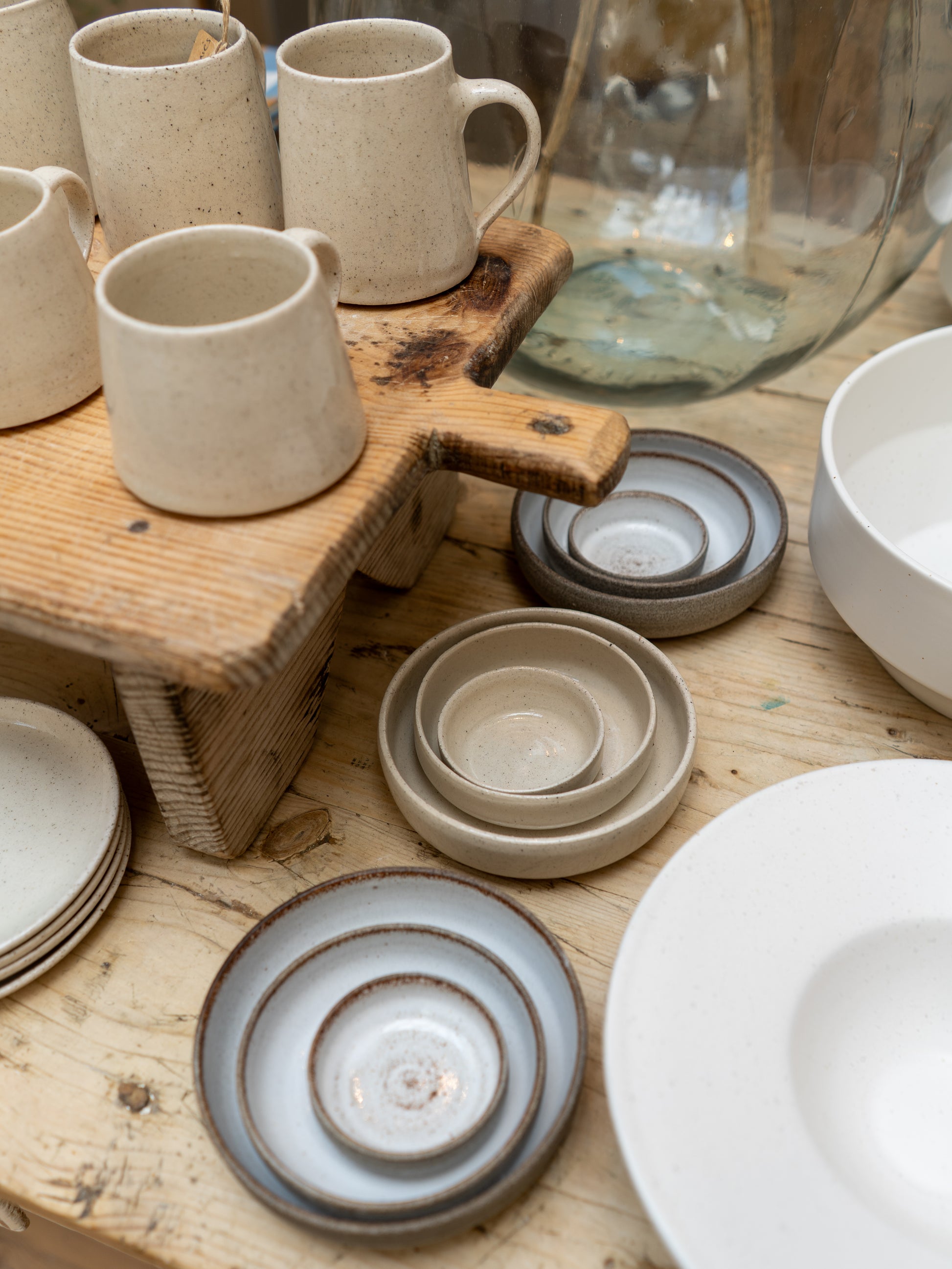 Collection of ceramic mugs, bowls, and plates on a wooden surface.
