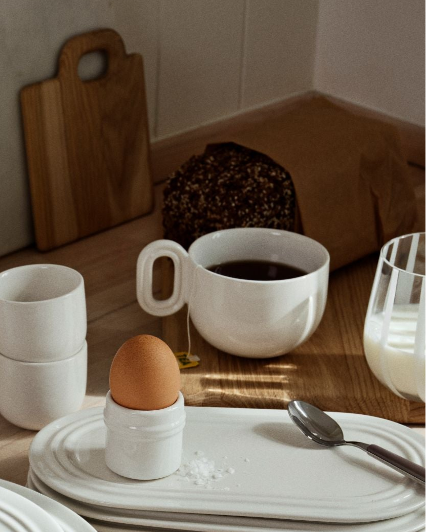 White ceramic plates and cups on a wooden table with kitchen items in the background.
