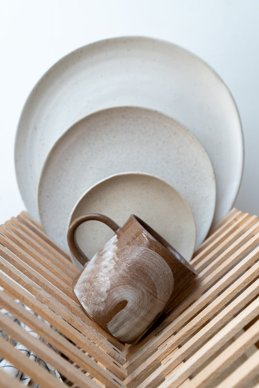 Ceramic dishes including a mug, plate, and bowl on a wooden surface with a light background