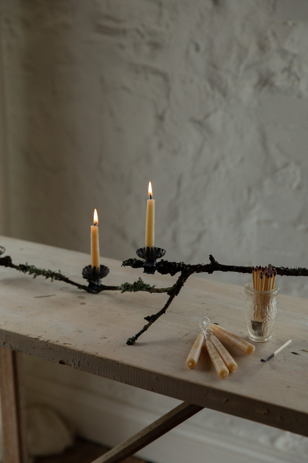 Candle holder made of branches with candles and matches on a wooden table.