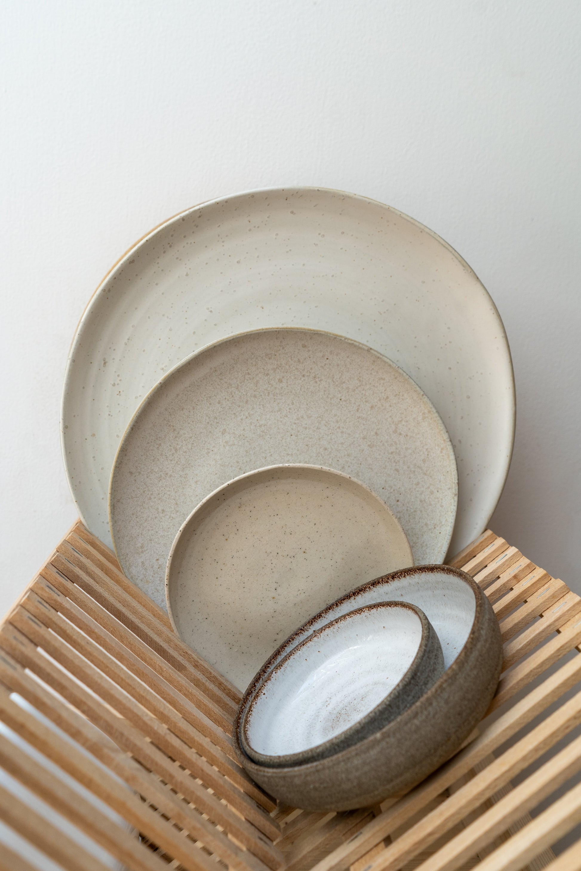 Collection of Pion plates next to a set of ceramic bowls on a wooden dish holder with a white background.