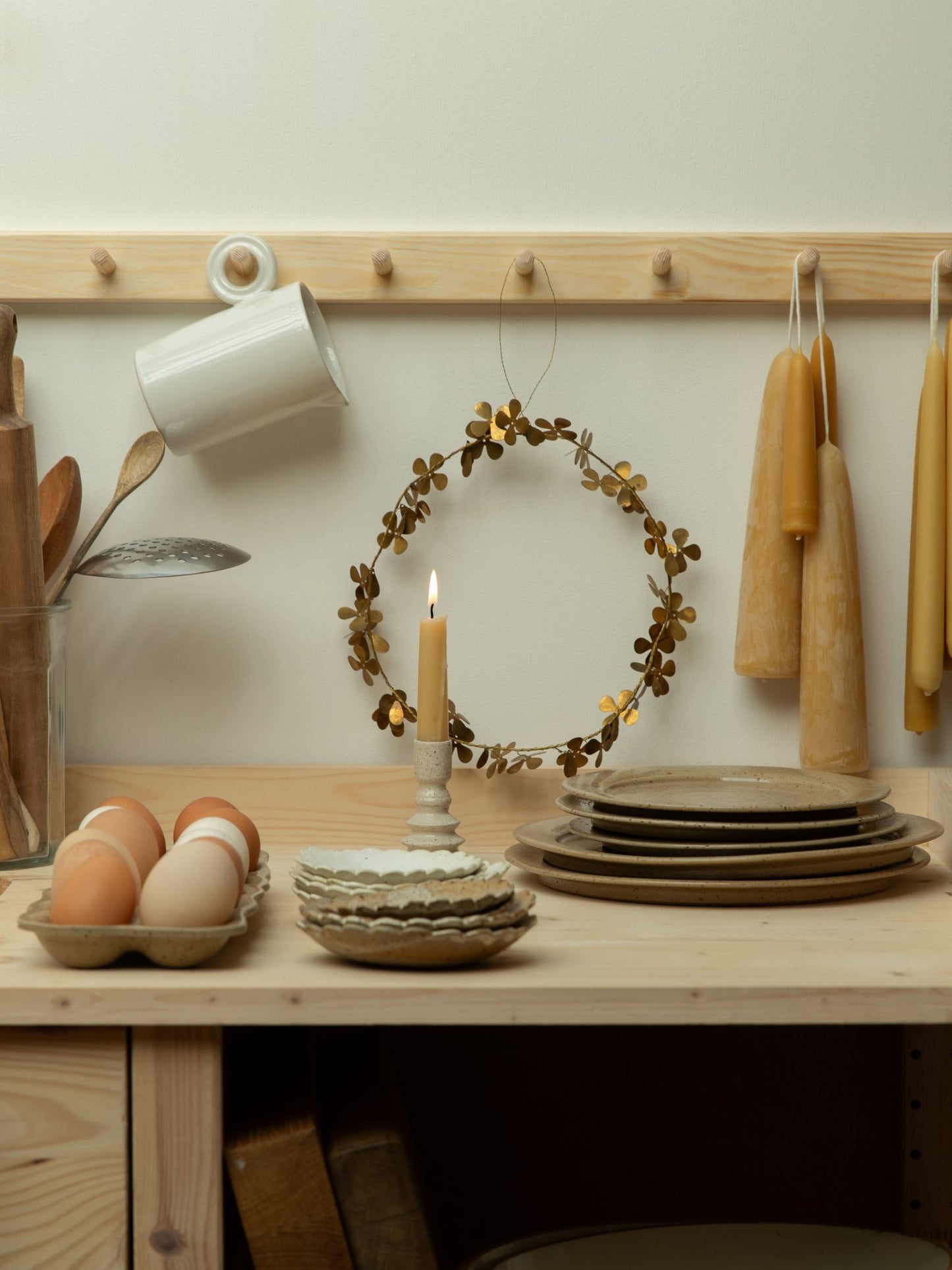Kitchen counter with plates, eggs, and a candle, with a wreath and hooks in the background.