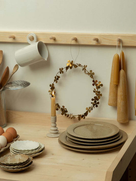 Decorative setup with ceramic plates, candles, and a wreath on a wooden surface.