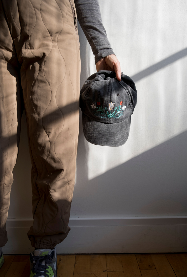 Person holding a cap with floral embroidery against a white wall