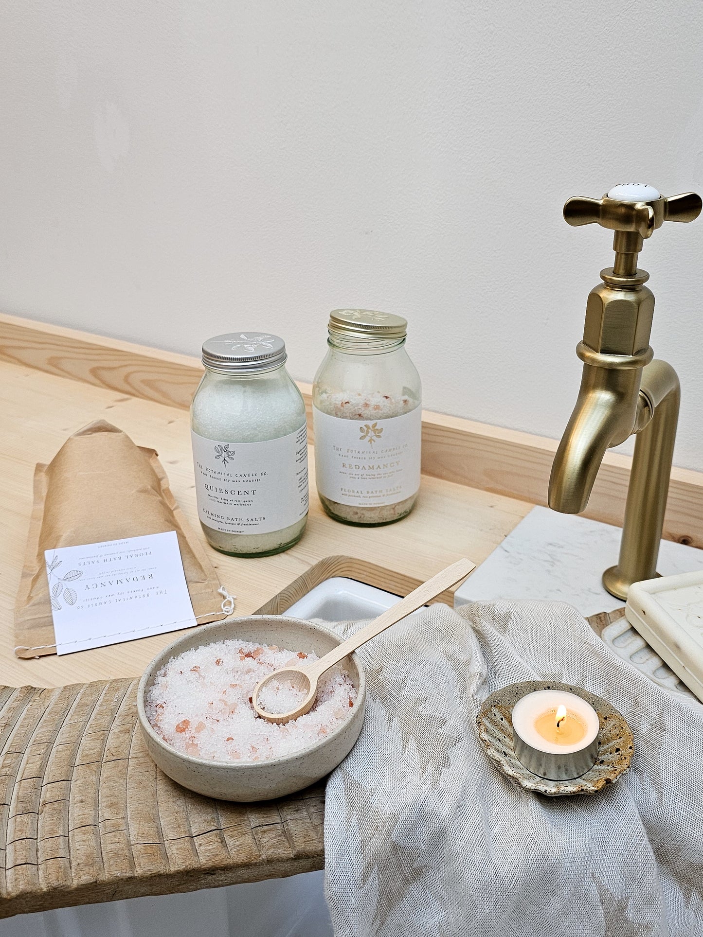Bath setup with jars, a bowl of bath salts, a candle, and a gold faucet.