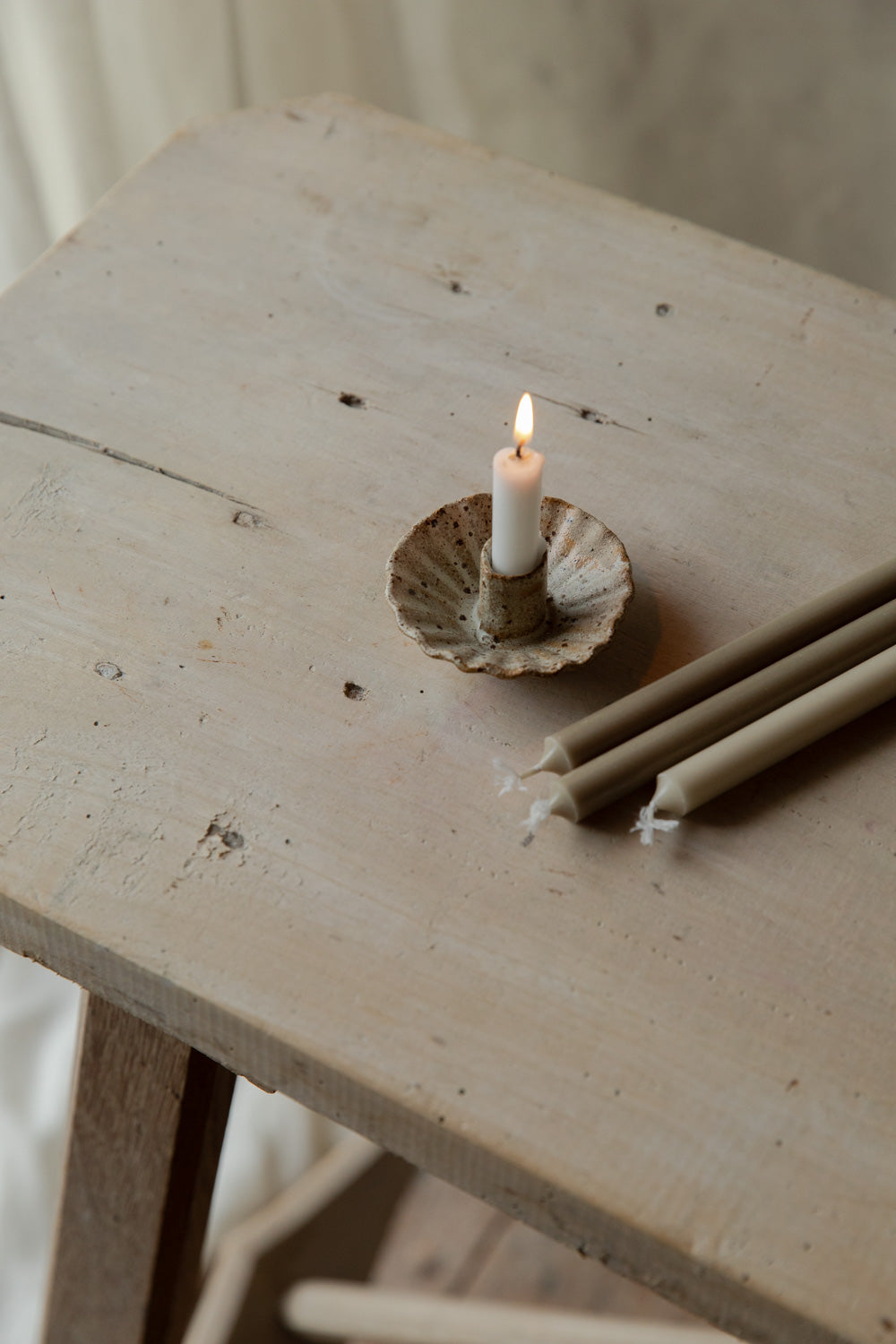 Candle in a handmade candle holder on a wooden surface with additional candles nearby.
