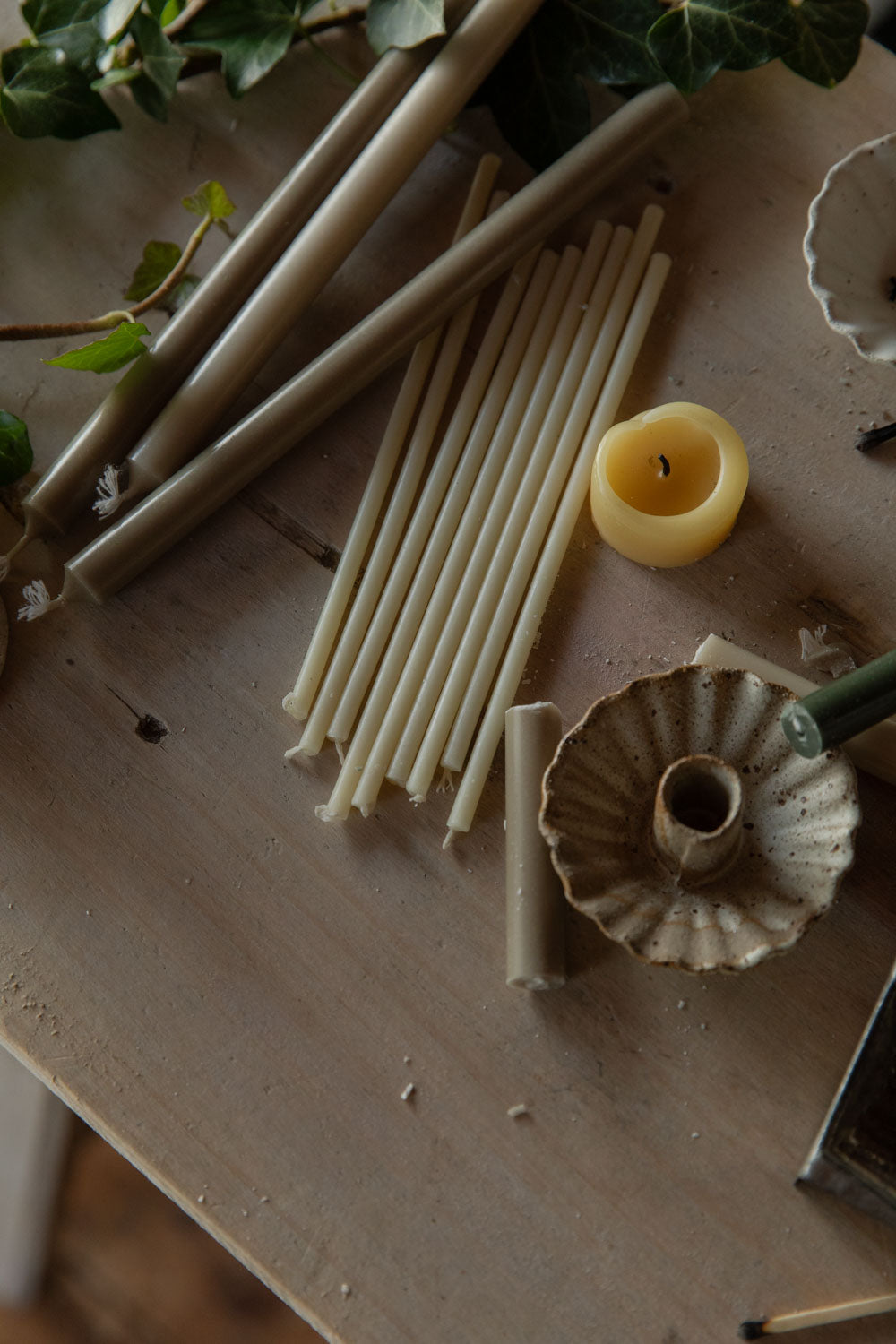 Scattered candles, candle holders and greenery on a wooden table.