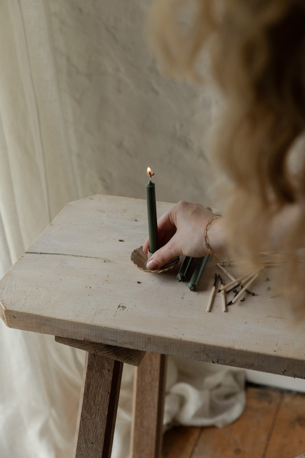 Person lighting a candle on a wooden table with a blurred background.