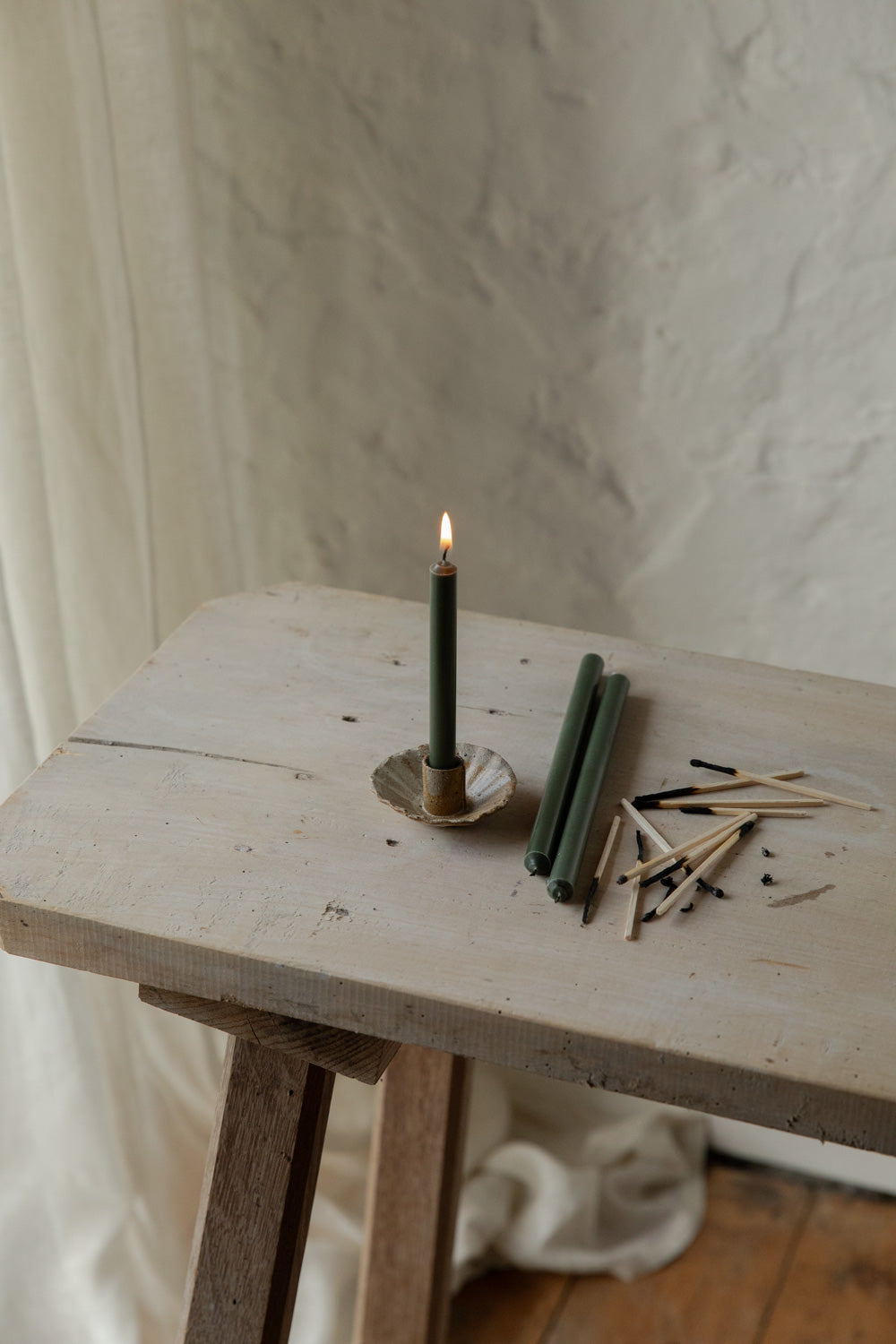 Small candle with matches on a wooden surface against a textured wall.