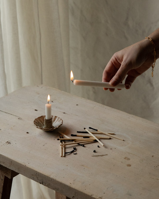 Hand lighting a candle on a rustic wooden table with scattered matches.