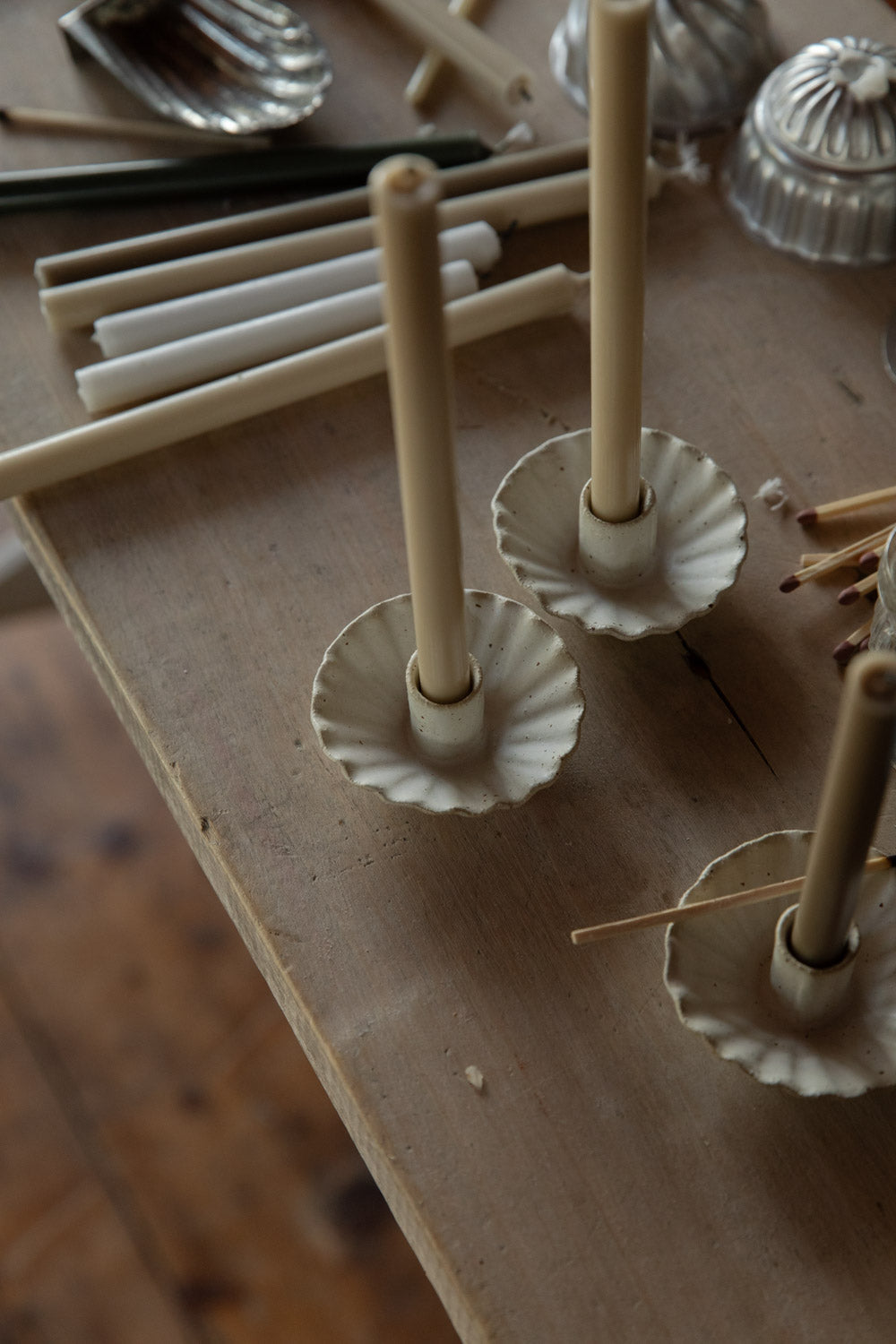 Handmade white candle holders on a wooden surface with candles and additional decor items.