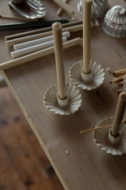 Handmade white candle holders on a wooden surface with candles and additional decor items.