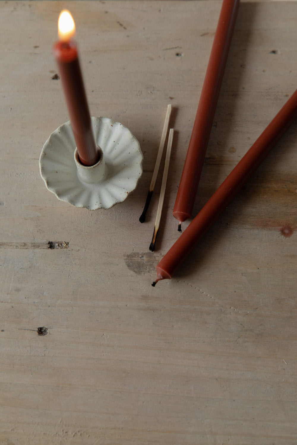 Red candle in a handmade white fluted candle holder with matches on a wooden surface.