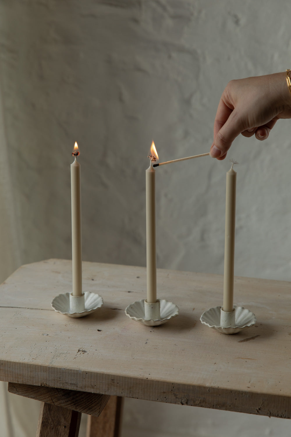 Person lighting a candle using a match on a wooden table with a neutral background.