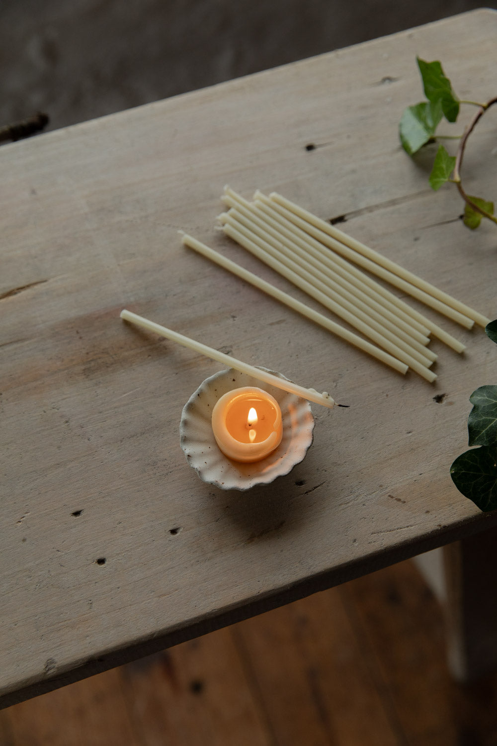Small candle in a fluted ceramic dish with wicks on a wooden surface.