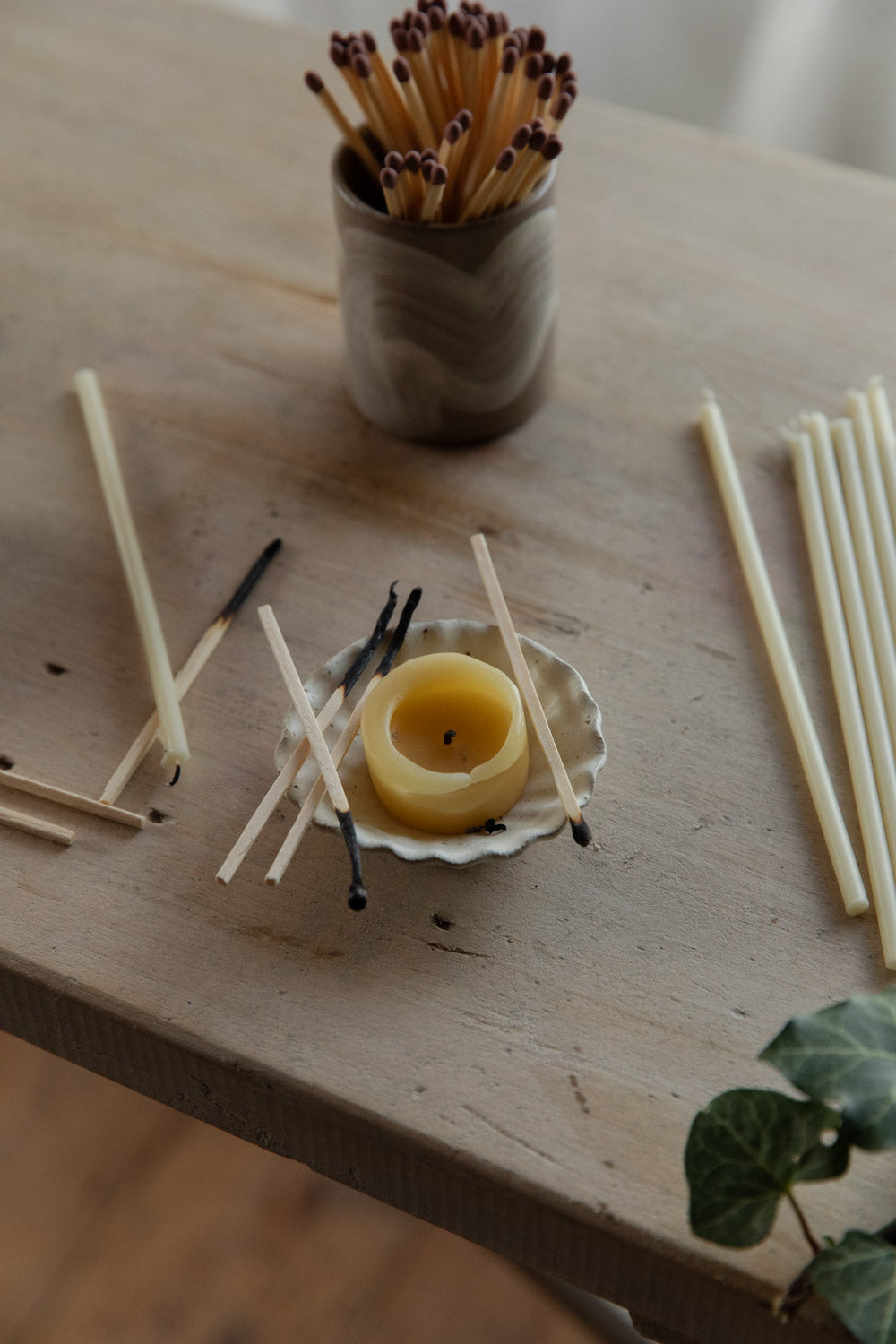 Matches and a small candle in a fluted white dish on a wooden surface with a blurred background.
