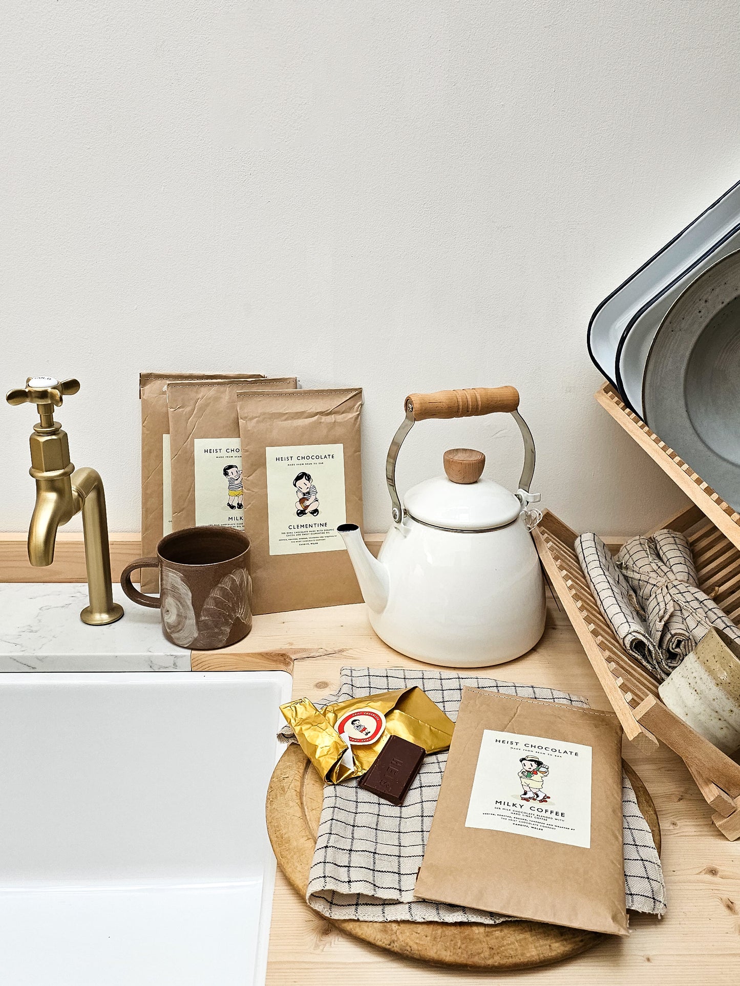 Kitchen setup with a teapot, coffee mug, and chocolate packaging on a wooden surface.