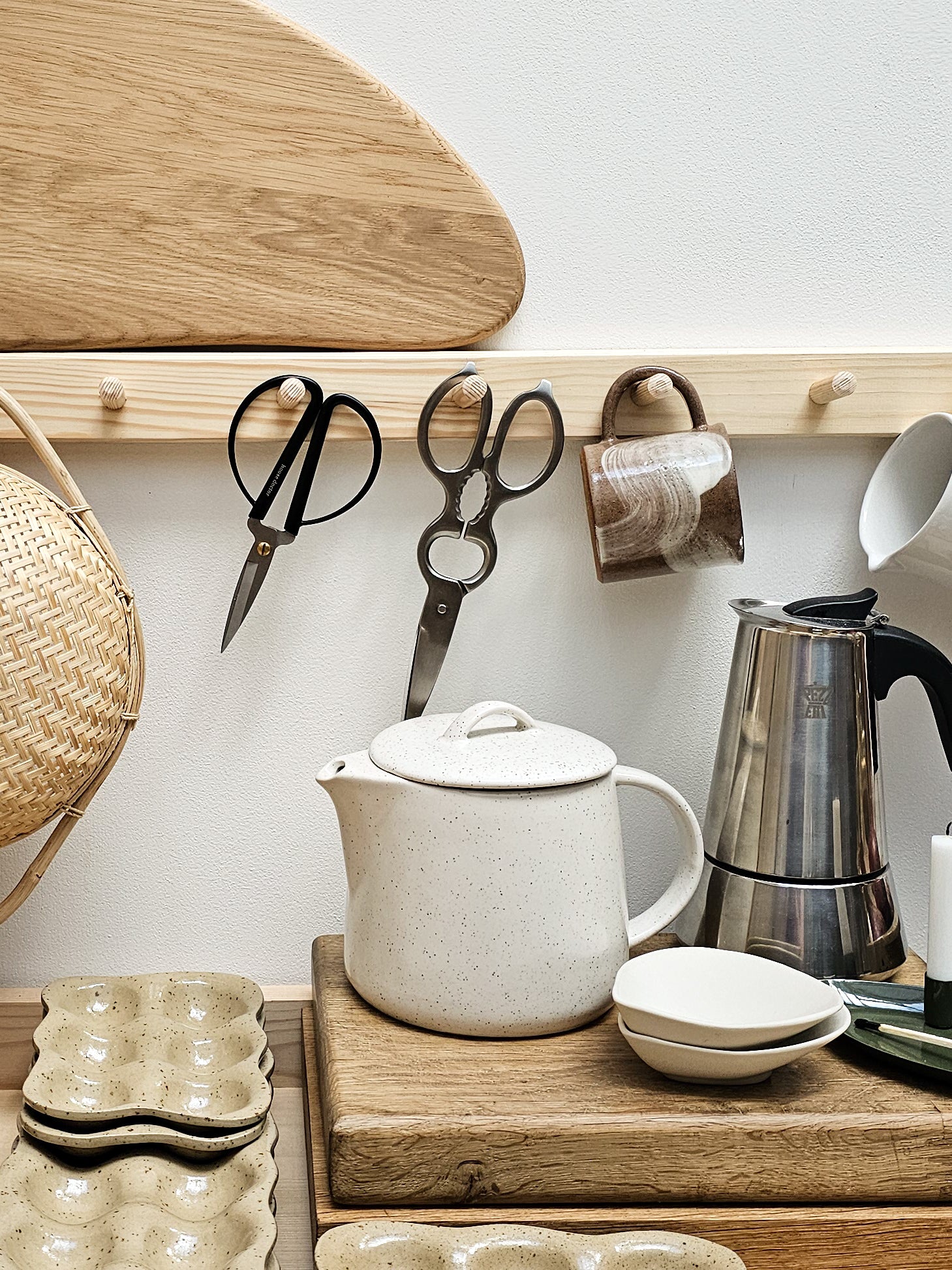 Kitchen counter with a teapot, kettle, and various kitchen items on a wooden shelf.