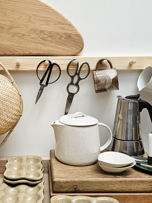 Kitchen counter with a teapot, kettle, and various kitchen items on a wooden shelf.