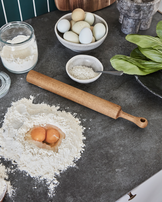 Ingredients for baking on a dark surface with a rolling pin and flour.