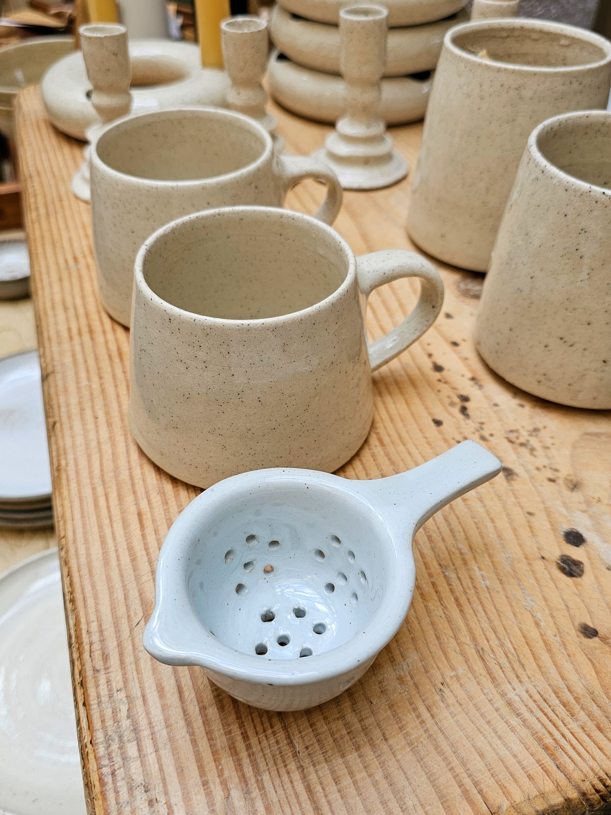 Ceramic mugs and a strainer on a wooden surface