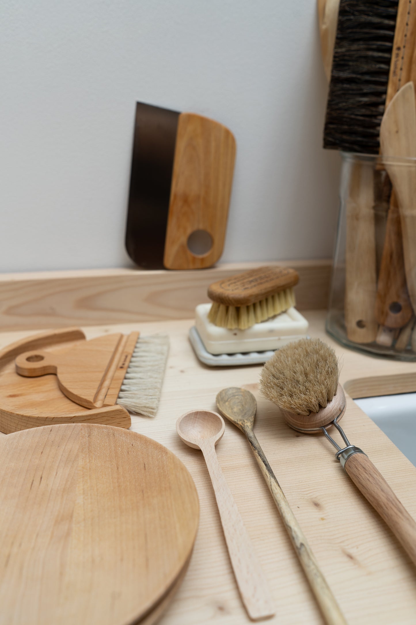 Set of wooden utensils including a nail brush, cutting board, spoons, and scrub brushes on a light wooden surface.