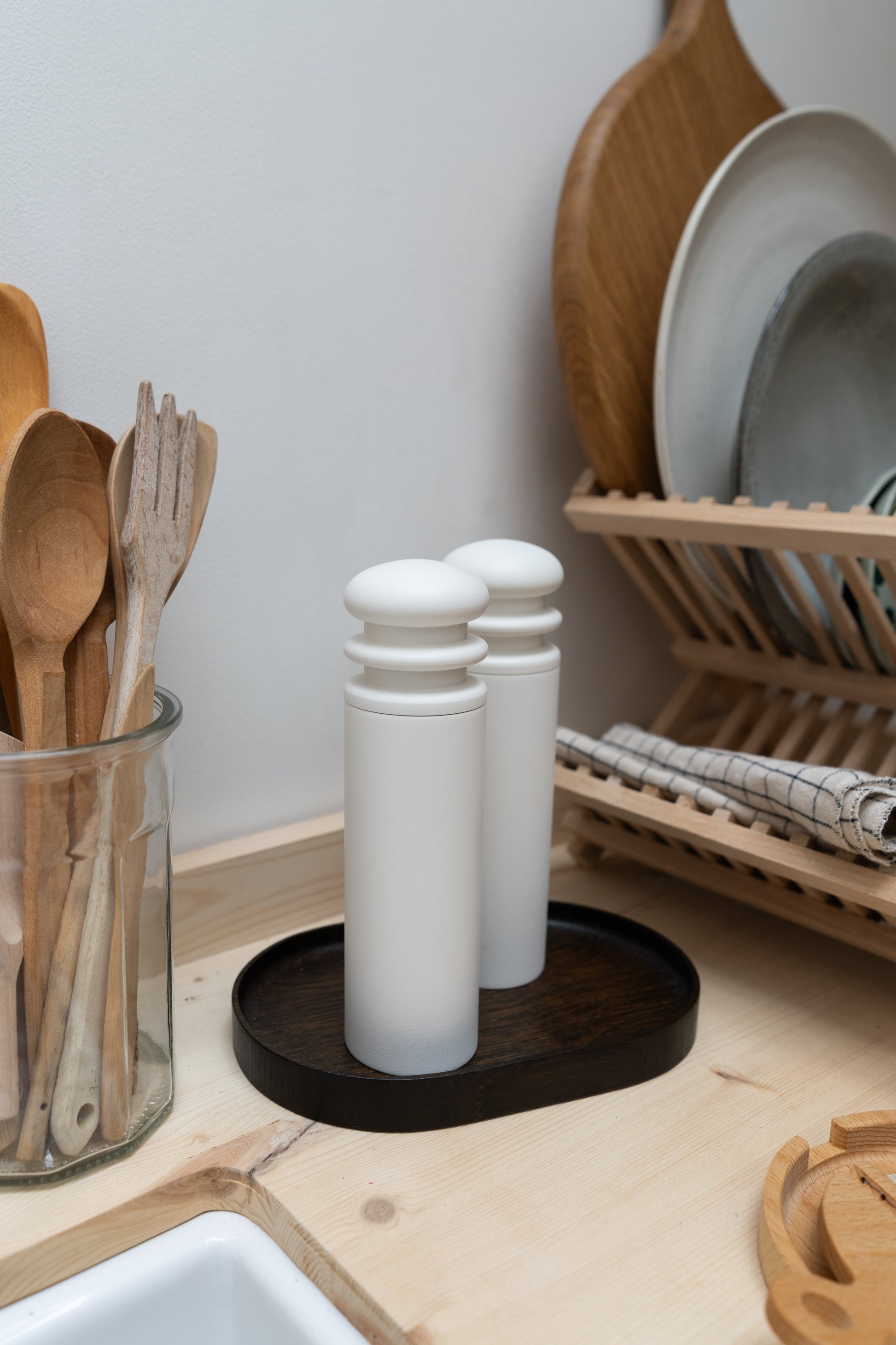 White salt and pepper shakers on a dark wooden coaster with a kitchen counter background.