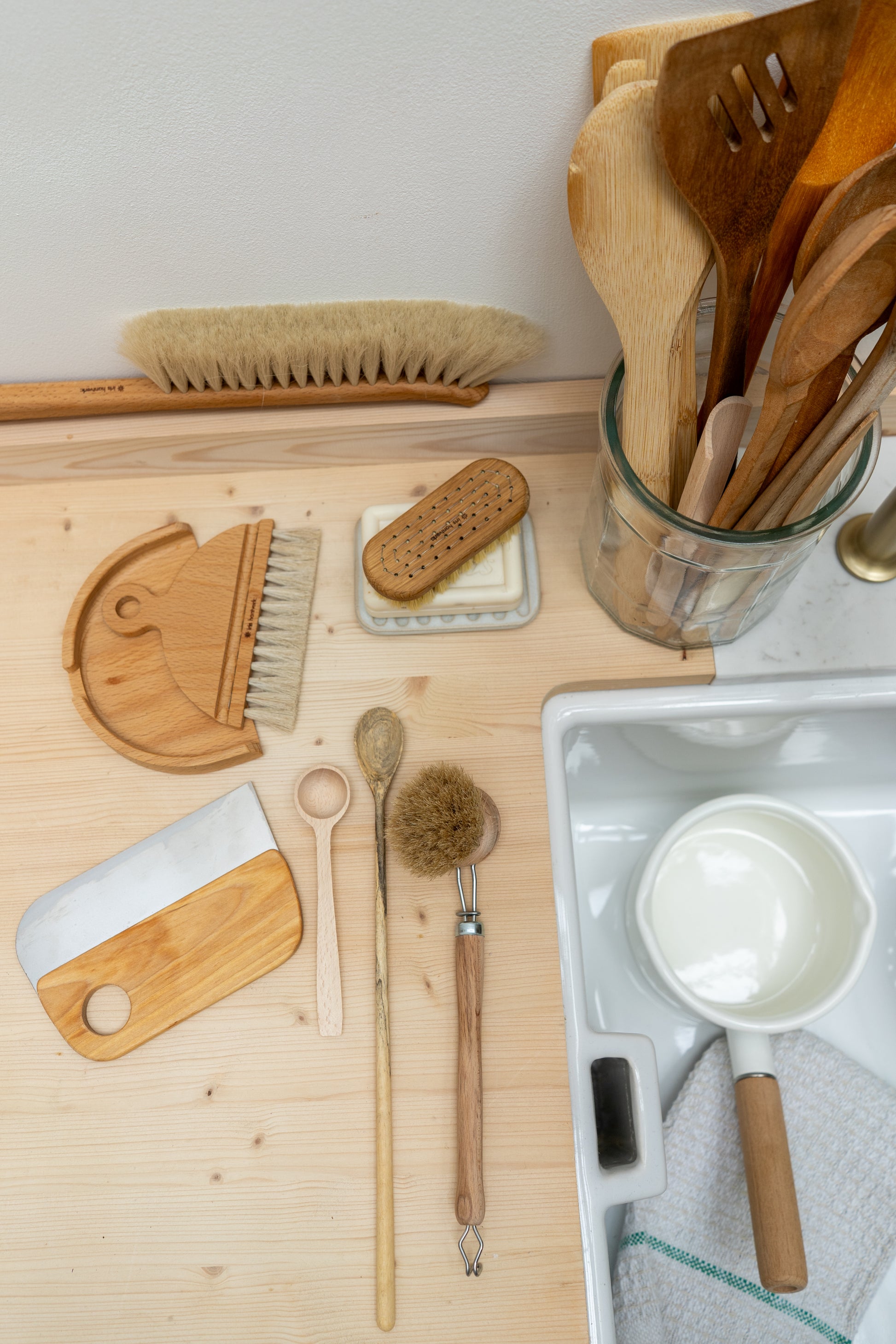 Set of wooden kitchen utensils and cleaning tools on a wooden surface.