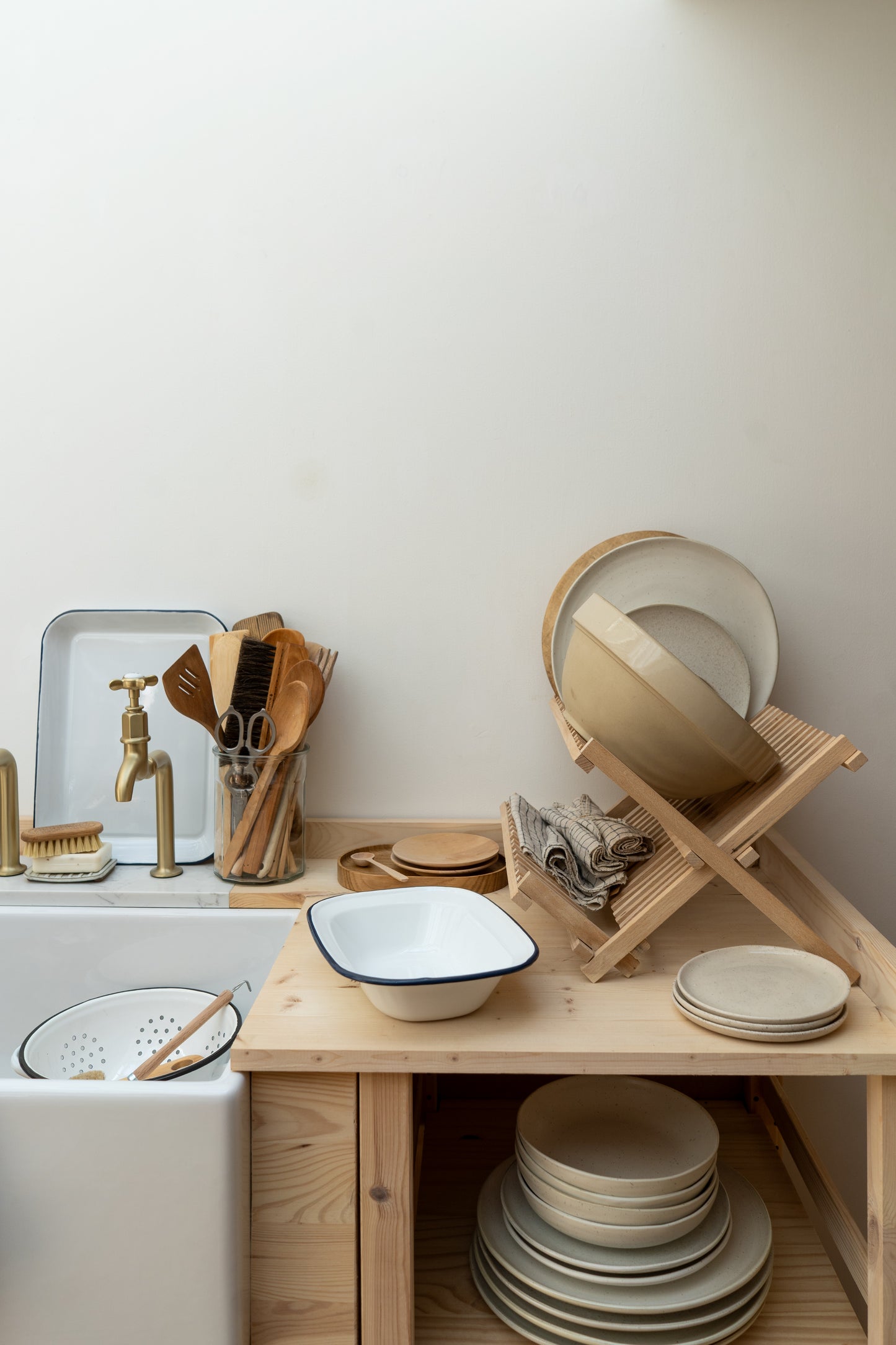Kitchen counter with dishes, a strainer, and a wooden rack against a white wall.