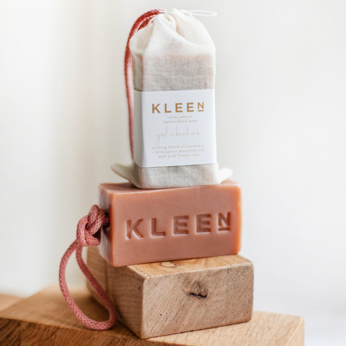Kleen soap bar and soap bag on a wooden block with a white background
