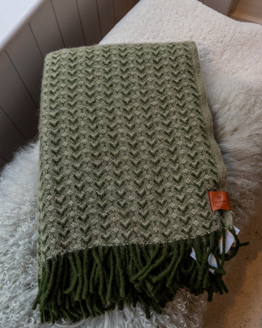 Woven green toned wool blanket folded on top of pale sheepskins.