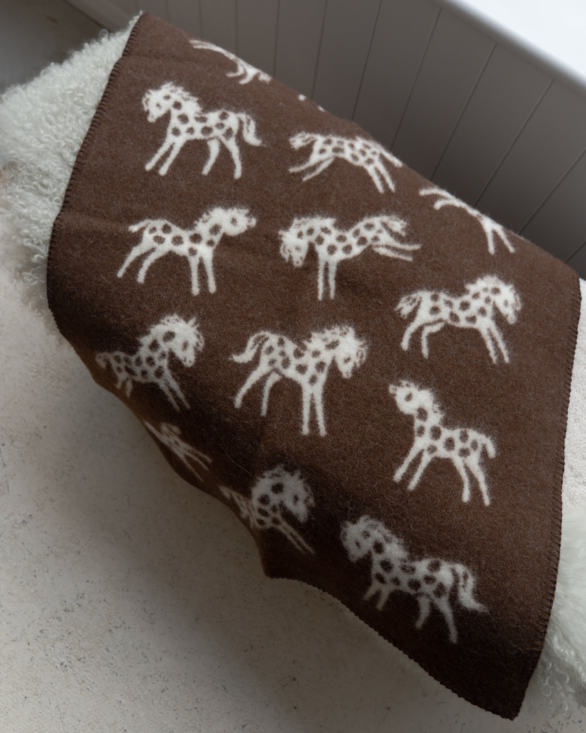 Brown blanket with white horse patterns draped over a white surface