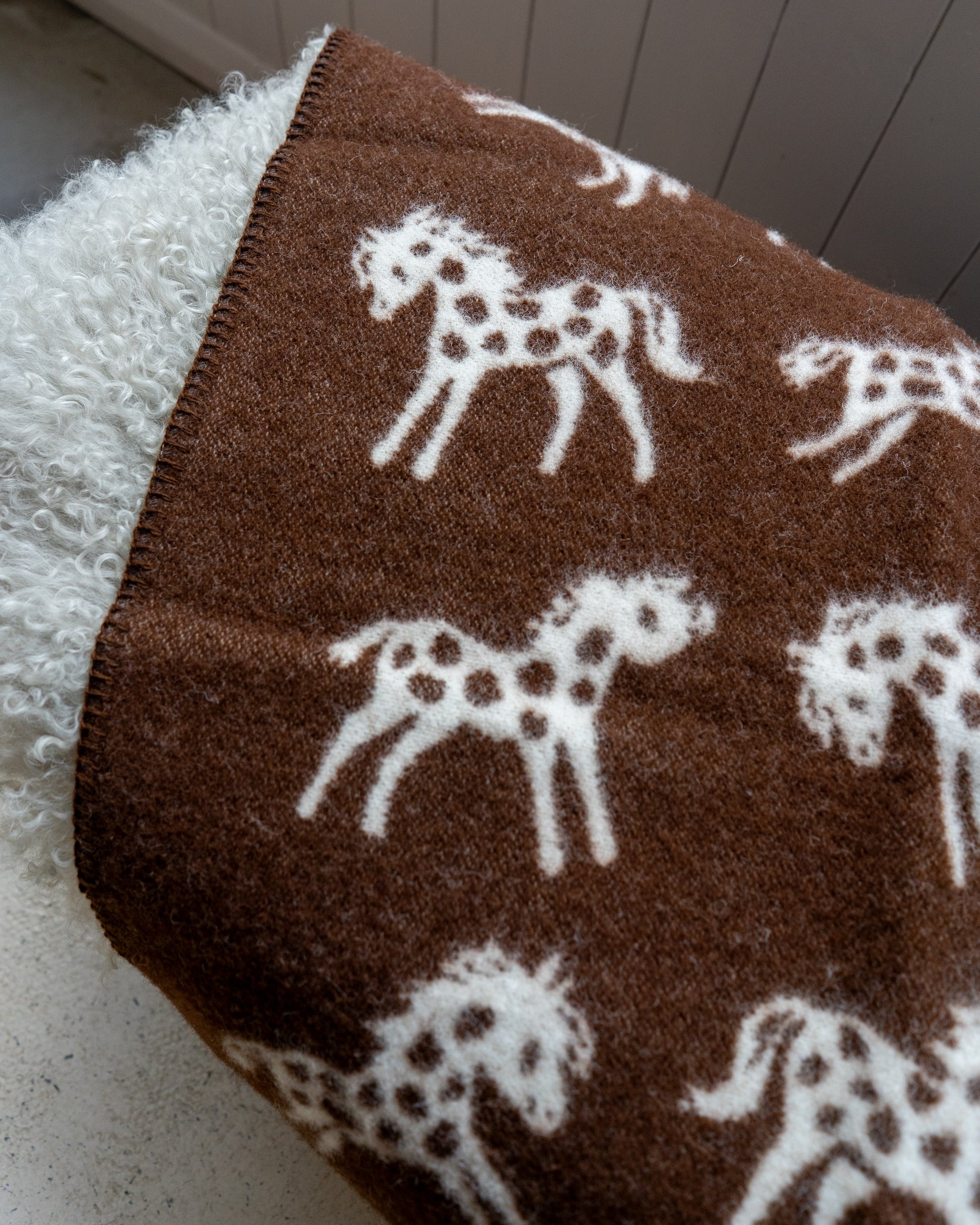 Brown blanket with white horse patterns on a textured surface