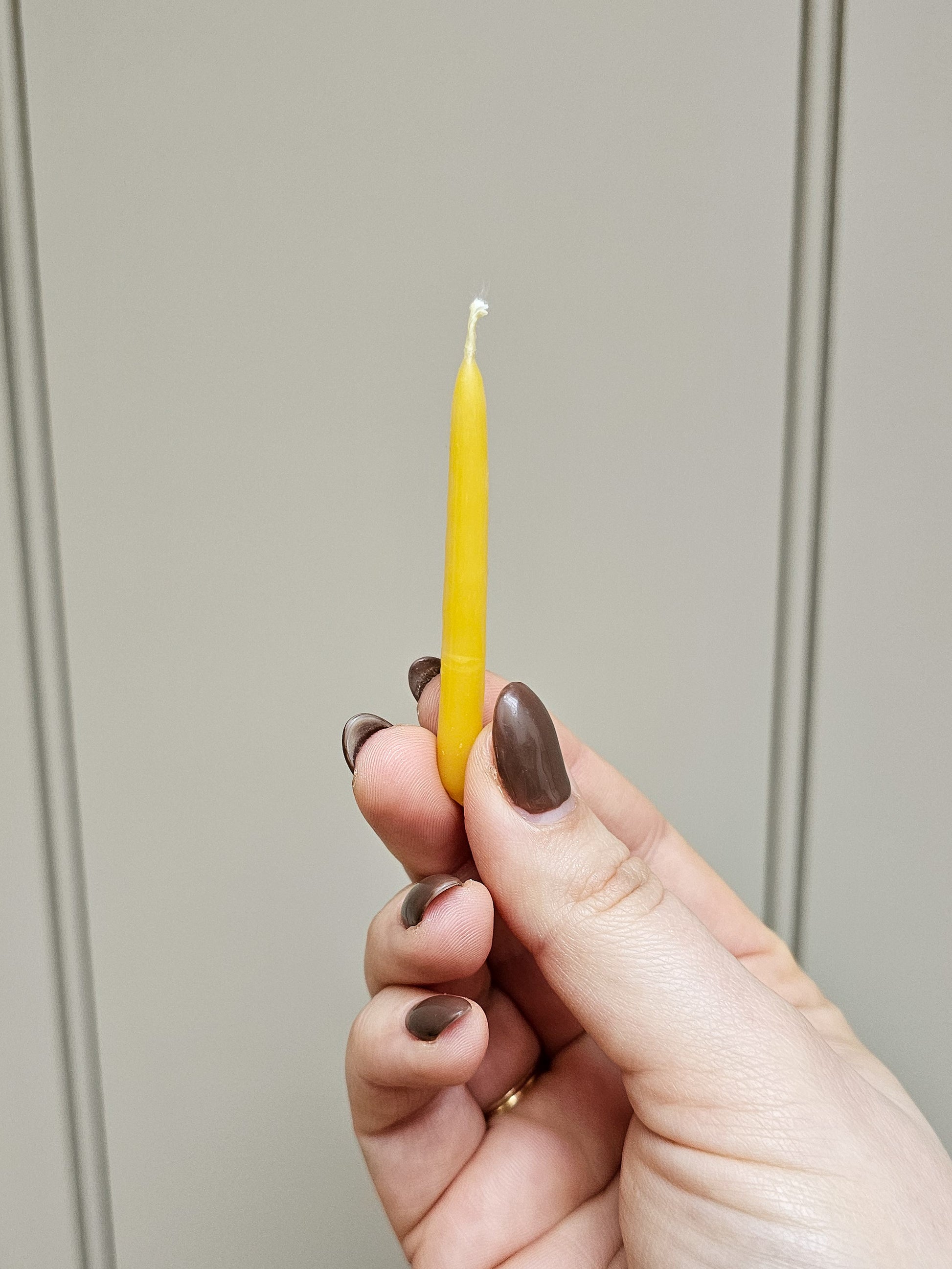 A mini candle held up in a woman's fingertips.