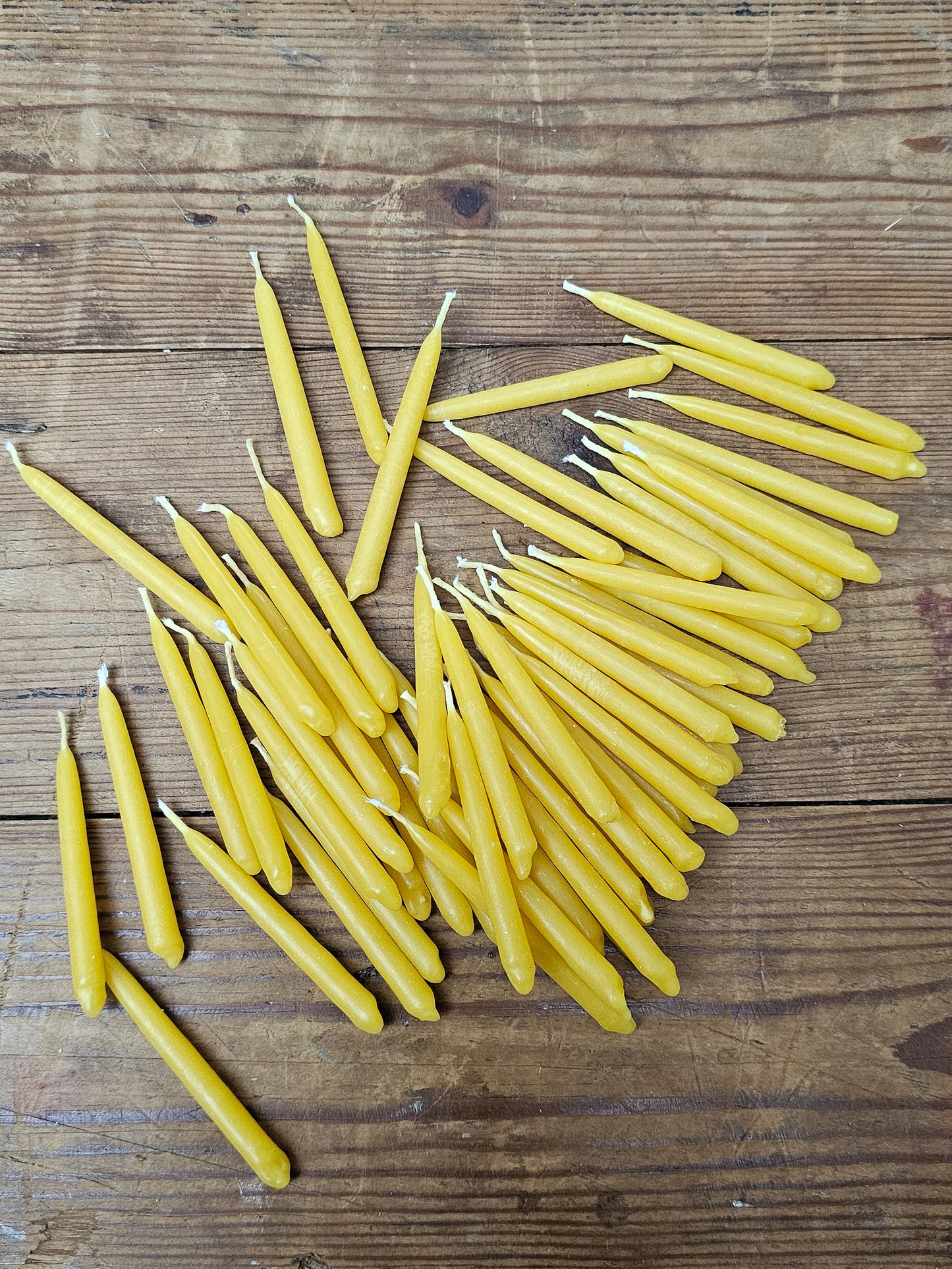 A scattering of mini beeswax candles on a wooden table, taken from a birds eye view. 
