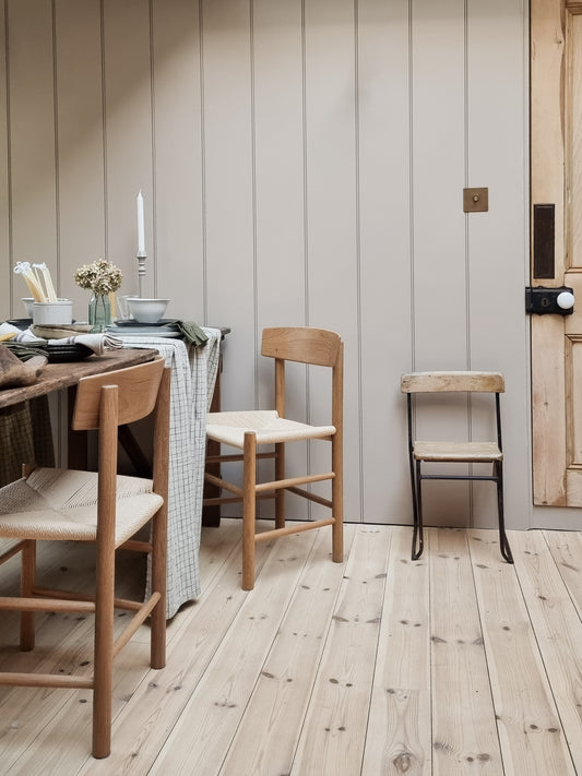 A classic Oak Shaker chair with a paper cord seat pad, placed in a room with wooden flooring and a dining set in the background.