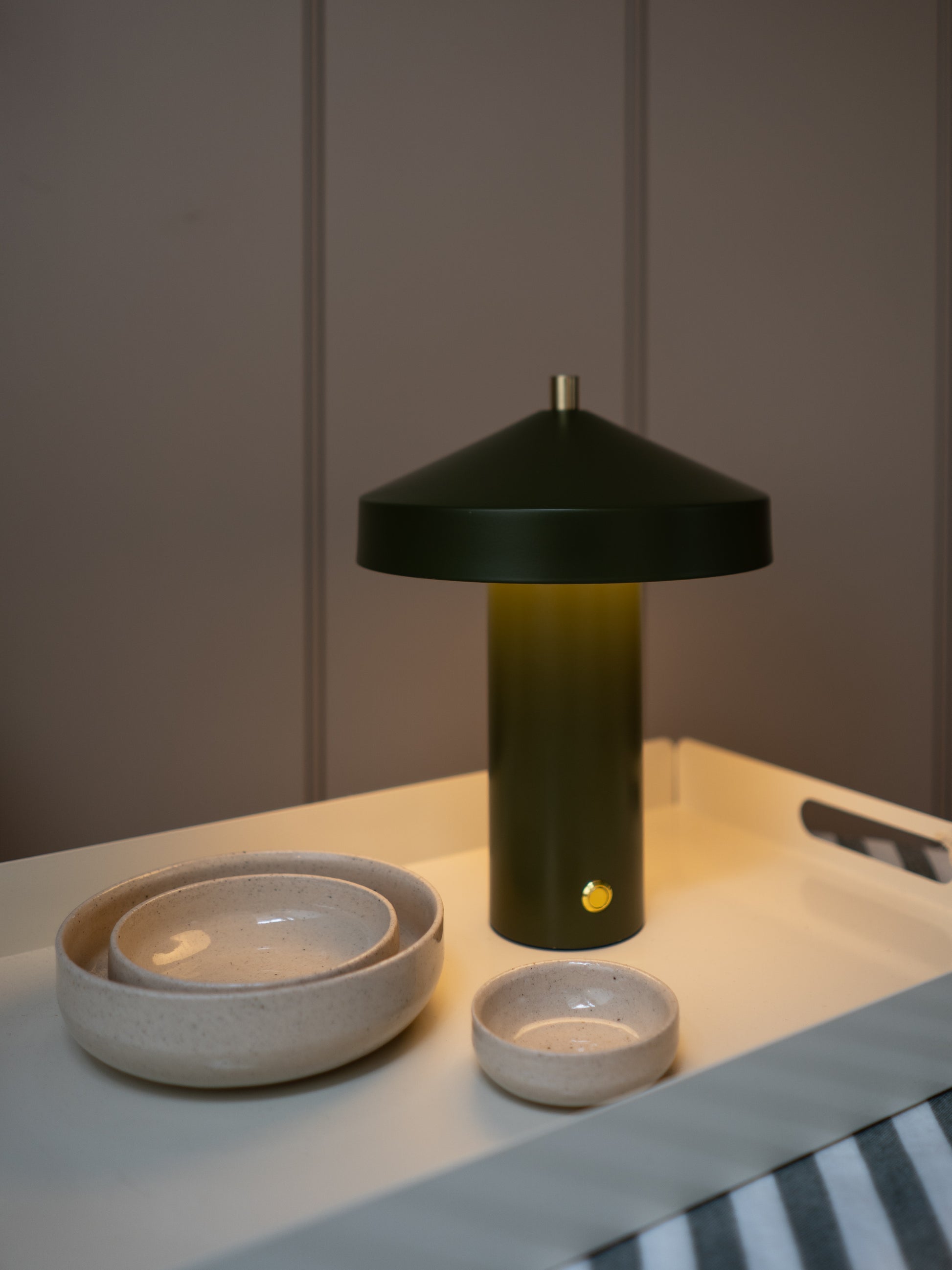 Green lamp with a cone-shaped shade on a table next to ceramic bowls.