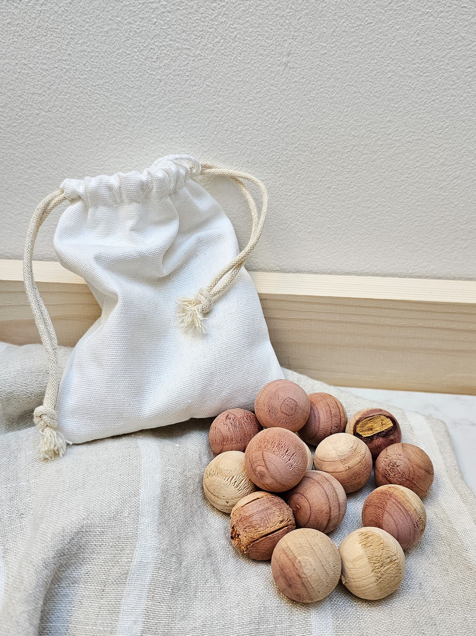 A white drawstring bag with a selection of red cedarwood moth balls spilling out onto a light surface.