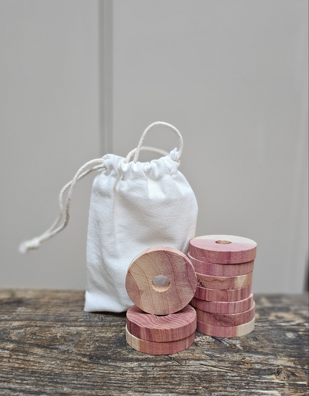 Two piles of red cedarwood moth discs stacked infront of a white cloth bag, placed on a wooden surface.