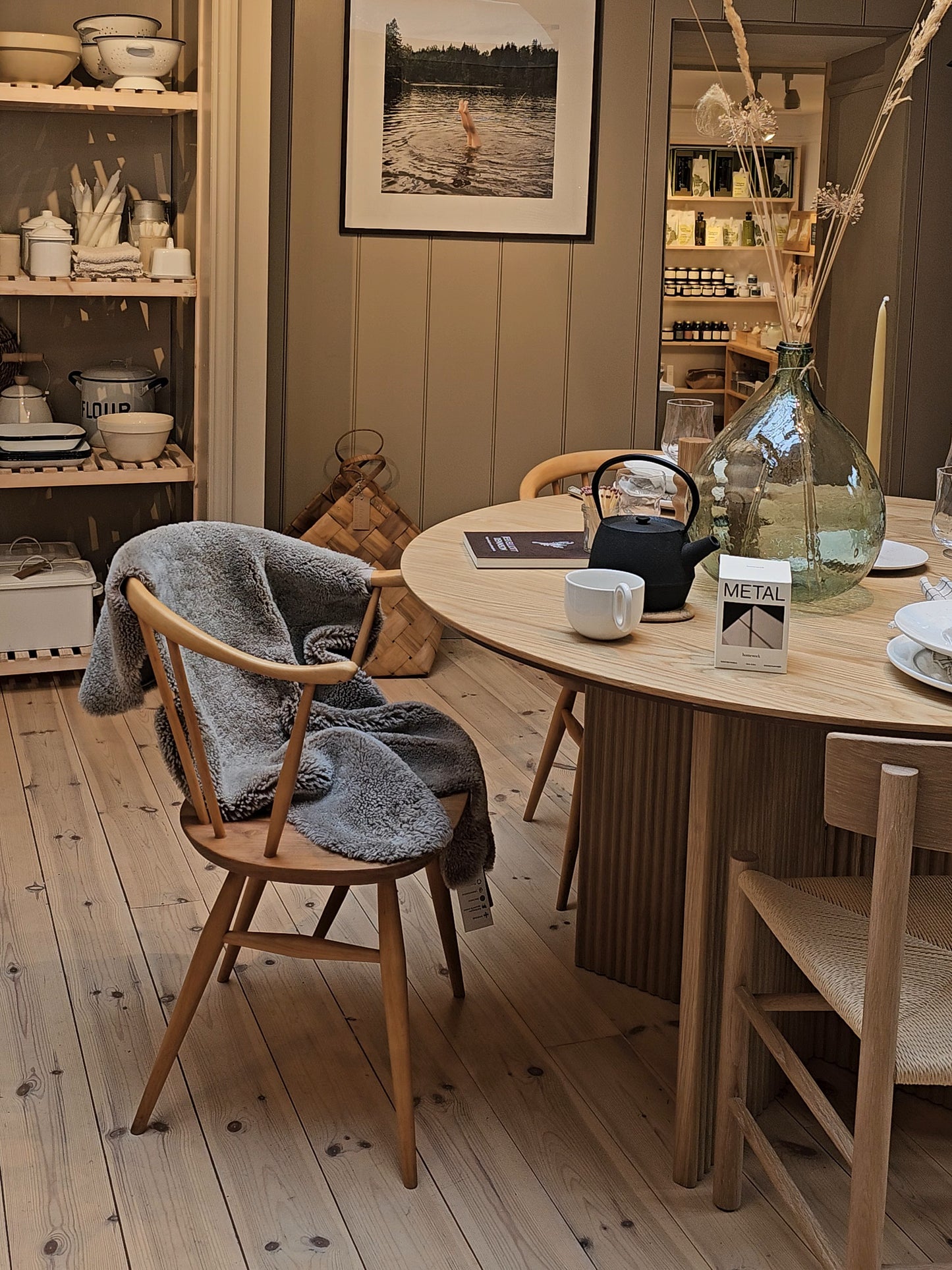 Dining room with wooden table and chairs, decor elements, and a picture on the wall. Taupe sheepskin rug draped over one of the chairs.