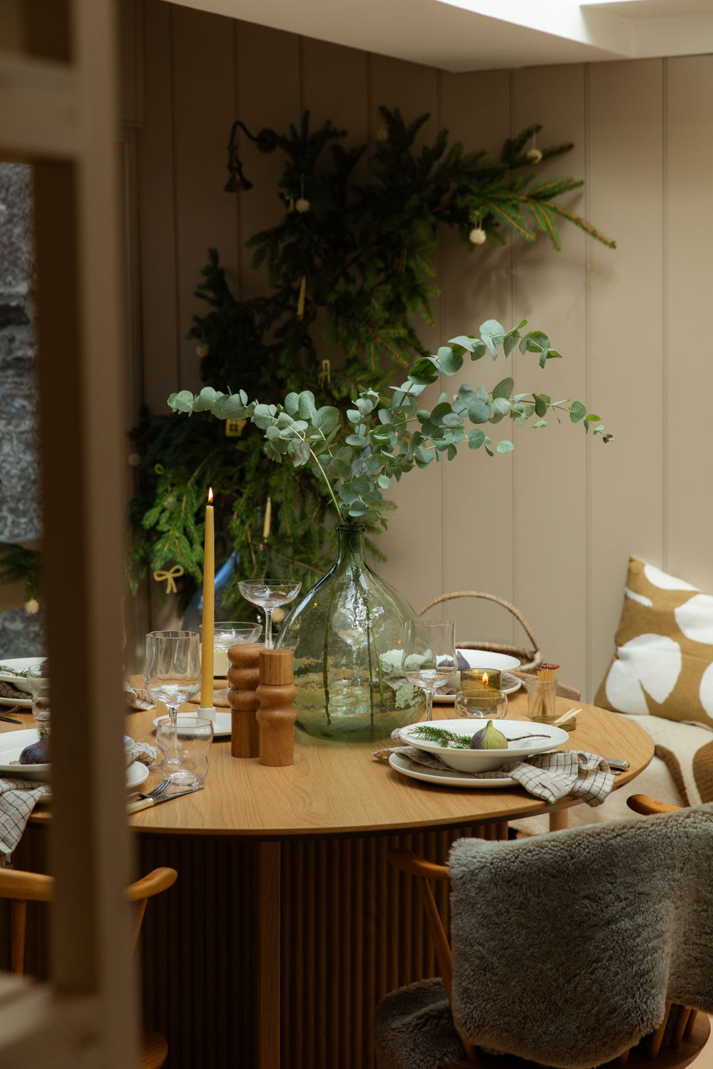 Dining room with a wooden table set for a meal, featuring candles, plates, and decorative elements. Taupe sheepskin rug is draped over one of the chairs.