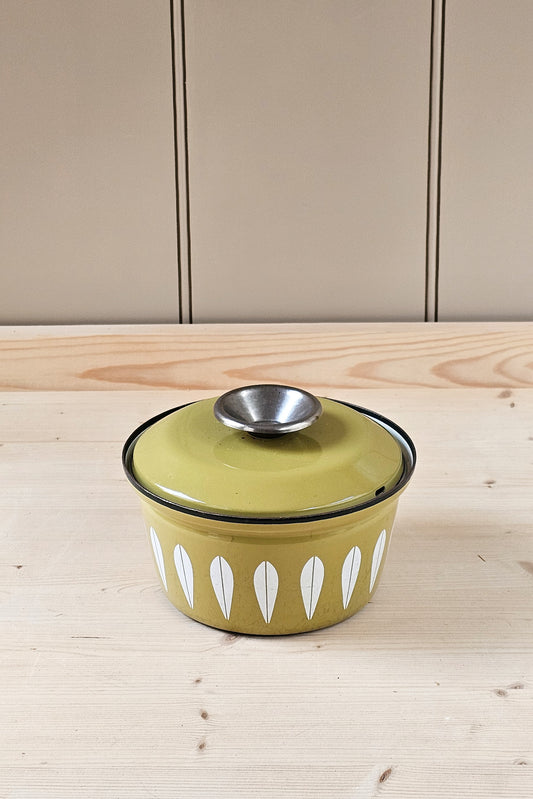 Green enameled pot with a silver lid on a wooden surface