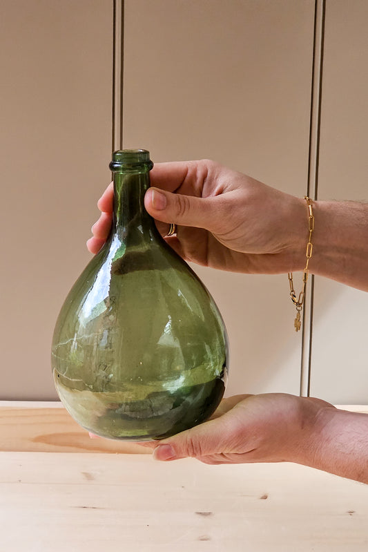 Hand holding a green glass bottle against a neutral background