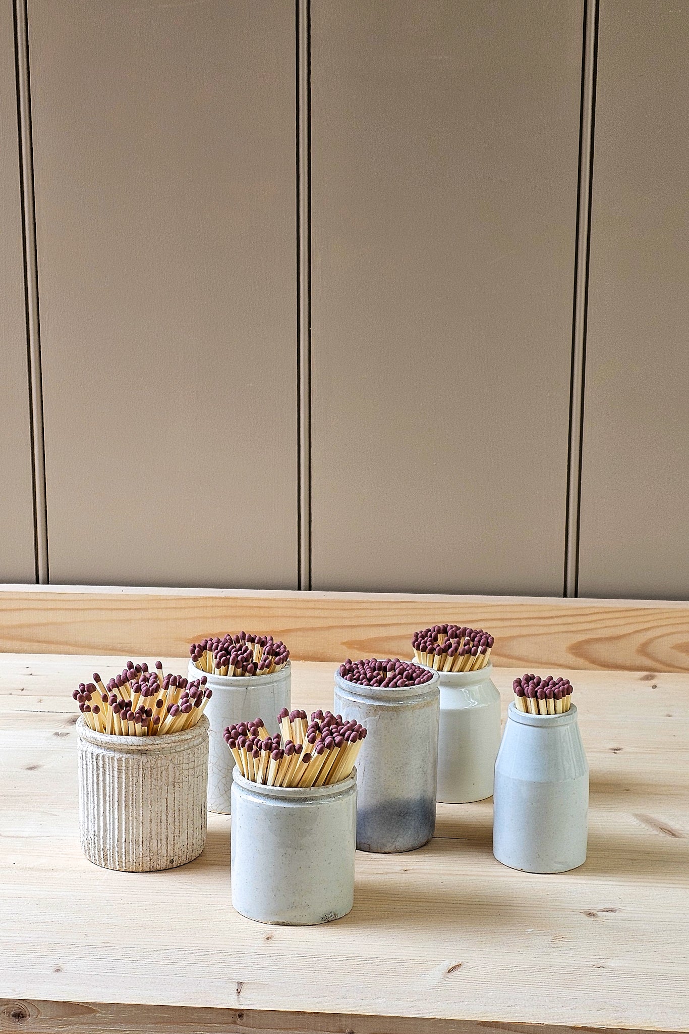 Set of small vintage ceramic pots with matches on a wooden surface against a neutral wall.