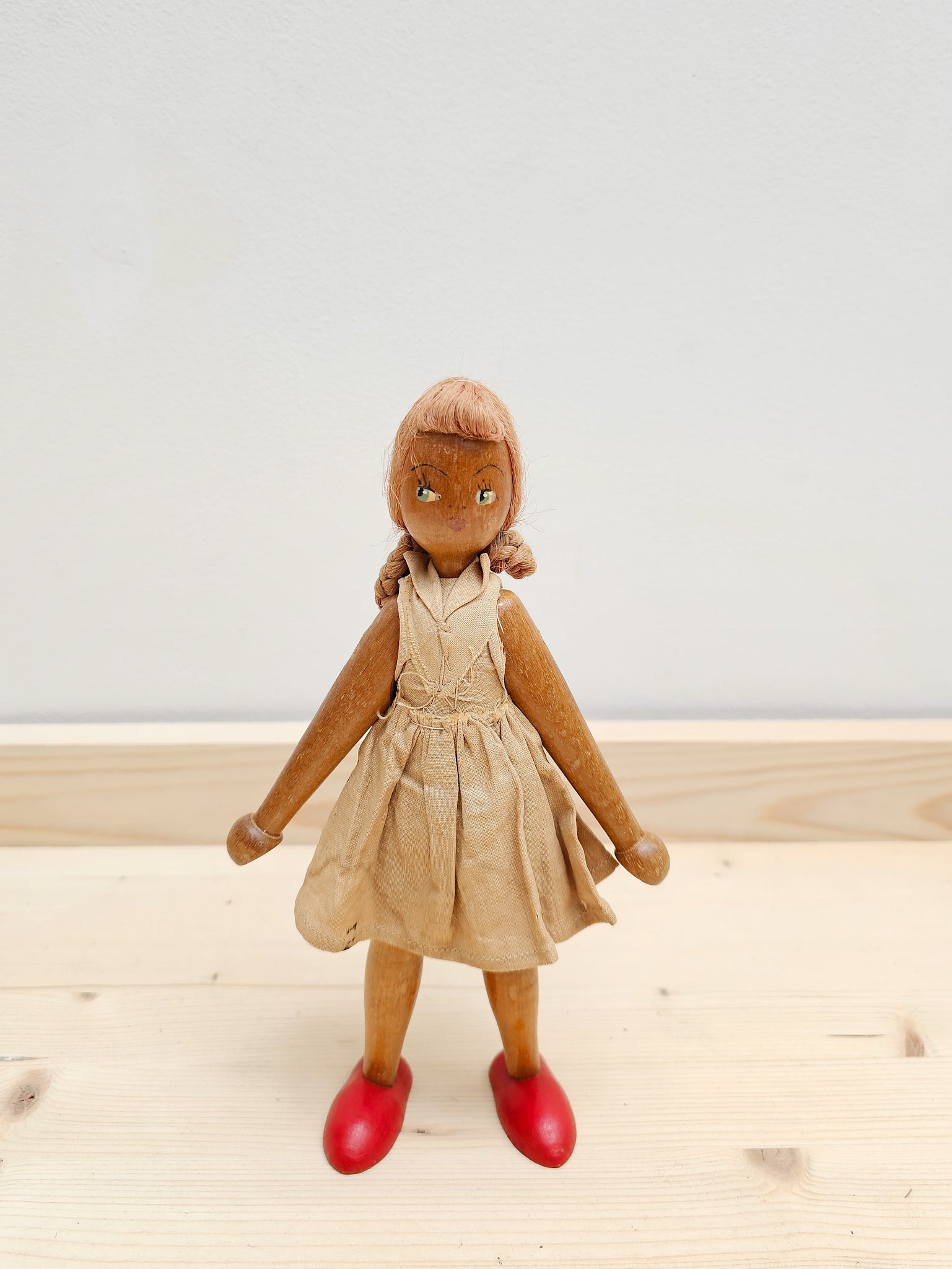 Vintage Polish wooden peg doll, wearing taupe handmade dress, beautifully painted face, against a white wall.